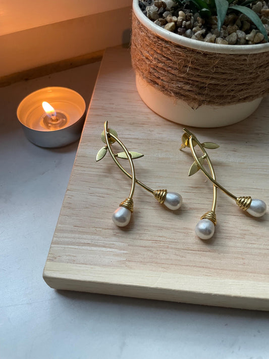 Freshwater pearl and brass leaf earrings arranged beside a candle and leaves