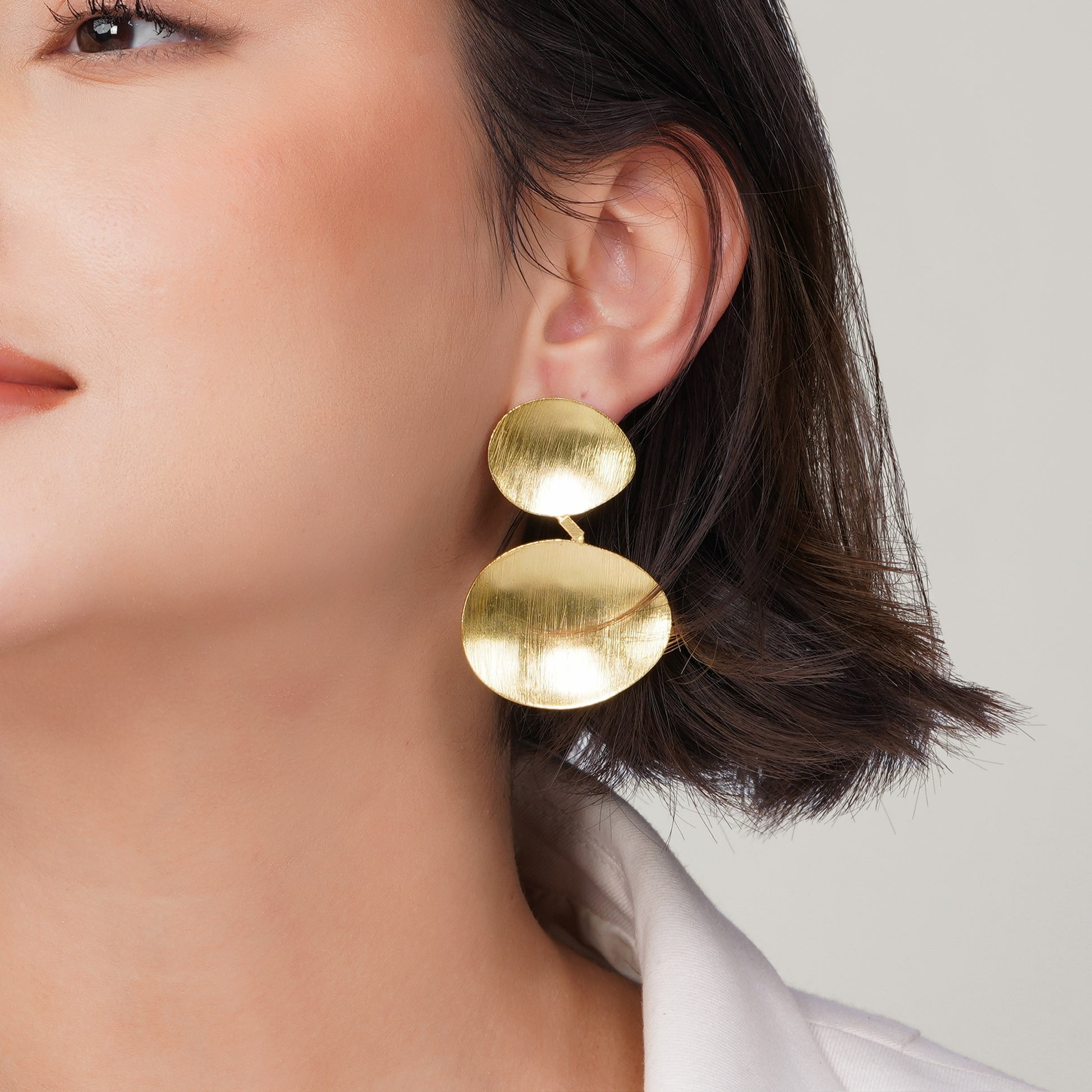 Close-up detail of a gold-plated organic disc earring featuring a matte brushed texture.